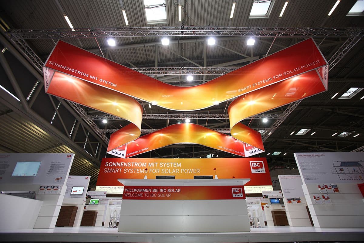 Detailfoto der x-förmigen Deckenaufhängung des Messestandes für IBS Solar auf der Intersolar München: Weiße Cuben und rot-gelbe Poster