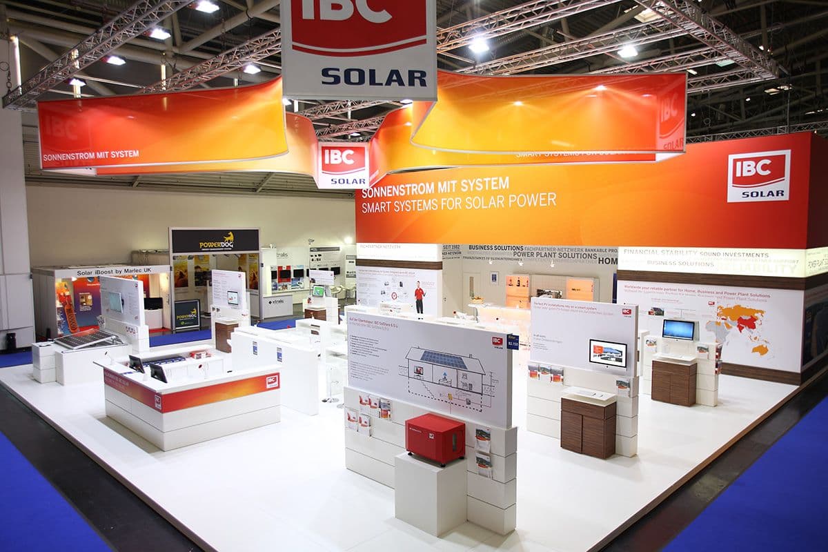 Foto des Messestandes für IBS Solar auf der Intersolar München: Weiße Cuben und rot-gelbe Poster
